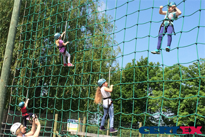 A rope net climbing wall made with steel wire rope and textile to be a combination rope, showing some people climbing up with height safety harnesses and laynards