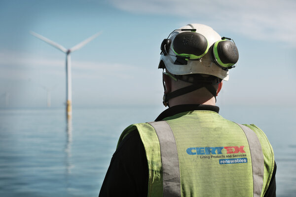 back of man wearing hi vis and helmet with wind turbine in the distance