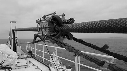 a steel wire rope on a taught line on an offshore vessel with a oil lubricating machine attached to it in black and white
