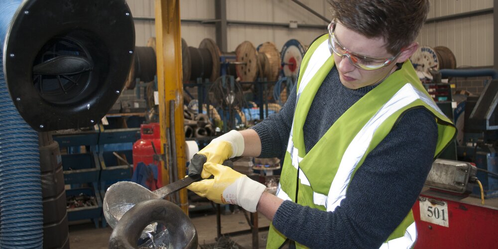 A picture of Rhys Webster. He is pouring white metal into a pear socket.