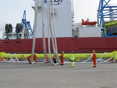 Some engineers managing a large lifting spreader beam and lifting slings next to an offshore vessel