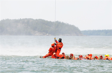 A few people floating in the sea while one is being air lifted away in a training exercise 