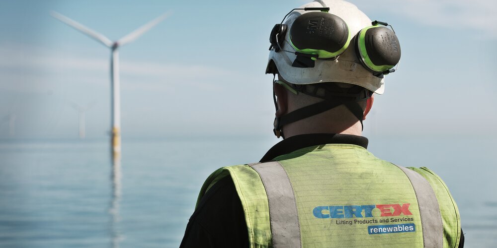 back of man wearing hi vis and helmet with wind turbine in the distance