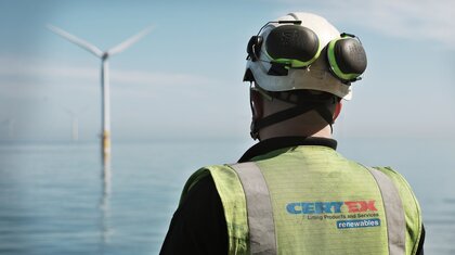 back of man wearing hi vis and helmet with wind turbine in the distance