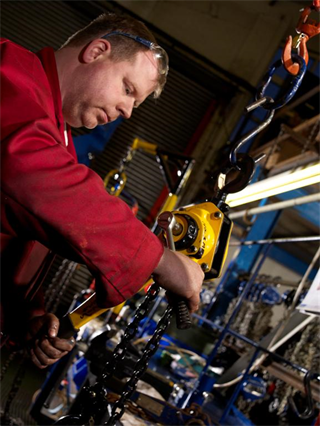Level Hoist Inspection and repair an image of a mans in red using a wrench to tighten a lever hoist which is being suspended on a hook